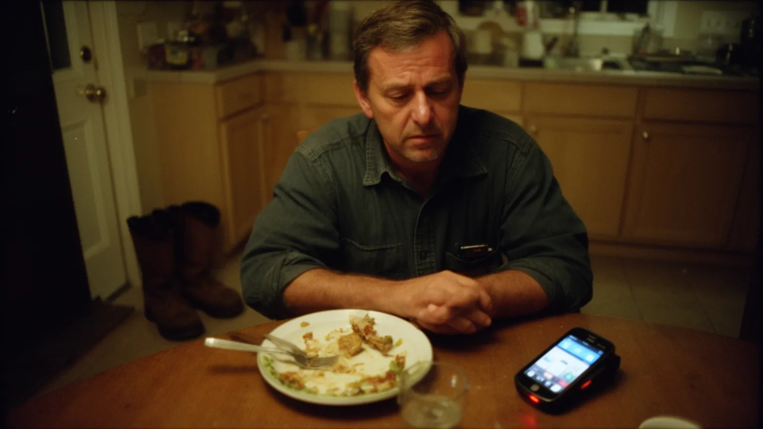HVAC technician at his kitchen table at night looking tired at his ringing phone next to his dinner